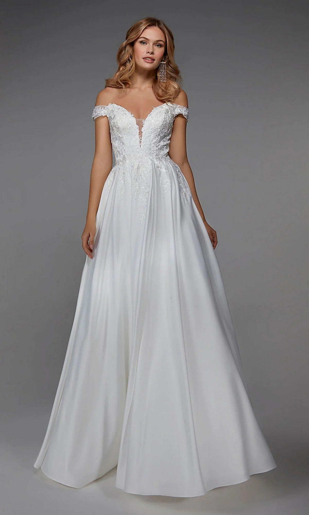 A woman in the Alyce 7034 Long White Dress, featuring an off-the-shoulder floral embroidered bodice and flowing satin a-line skirt, stands against a plain gray background.